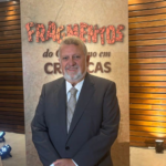 Autor durante o lançamento do livro Fragmentos do Cotidiano em Crônicas, em ambiente interno, posando diante do painel do evento