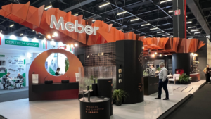 Estande da Meber Metais na Expo Revestir 2026 com estrutura ondulada em papel e exposição de torneiras e metais sanitários.